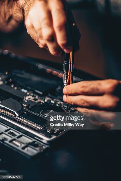 computer repair scene: hands-on laptop maintenance for technical support.macro view of a man’s hands tightening a screw on a laptop motherboard with a precision tool. electronics layout and fan clearly visible in sharp focus. - screwdriver stock pictures, royalty-free photos & images