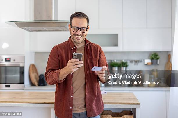 man interacting with a phone and credit card at home - debit card stock pictures, royalty-free photos & images
