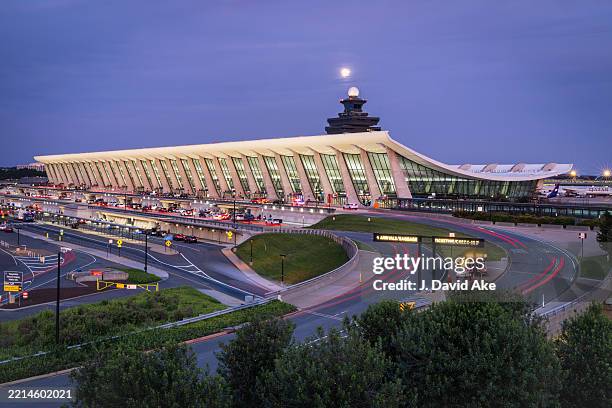 Traffic flows past the main passenger terminal at Washington Dulles International Airport at dusk on May 11 in Dulles, VA. The full moon can be seen...