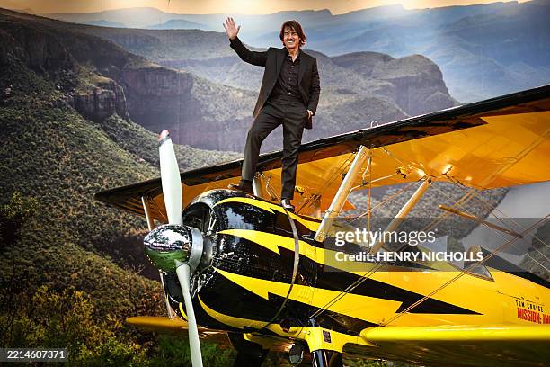 Actor Tom Cruise waves to the audience as he stands on a plane on the red carpet upon arrival for the Global Premiere of "Mission: Impossible - The...