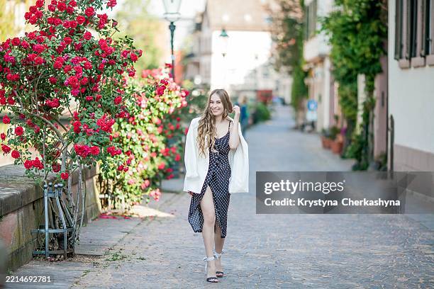 young beautiful woman walks in european city near blooming roses. - hair style collection stock pictures, royalty-free photos & images