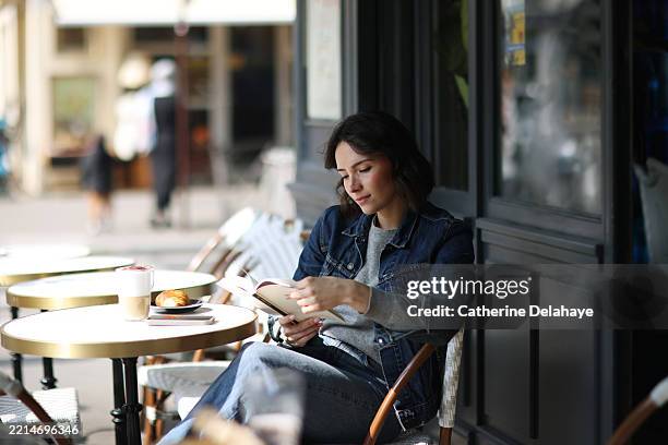 a young woman sitting on a parisian café terrace - paris cafe fotografías e imágenes de stock