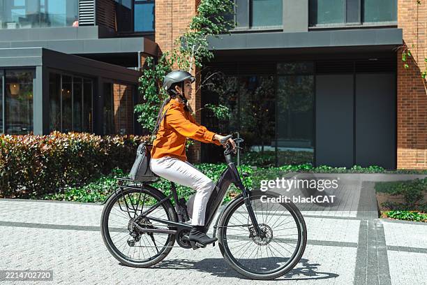 woman riding an electric bike outside modern urban building during the day - elcykel bildbanksfoton och bilder