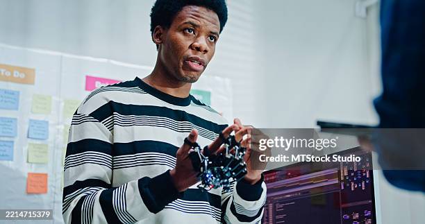 two male engineer software developers closely inspecting a robotic hand prototype working on development and coding tasks with integration in office. artificial intelligence and programming. - prosthetic equipment stock pictures, royalty-free photos & images