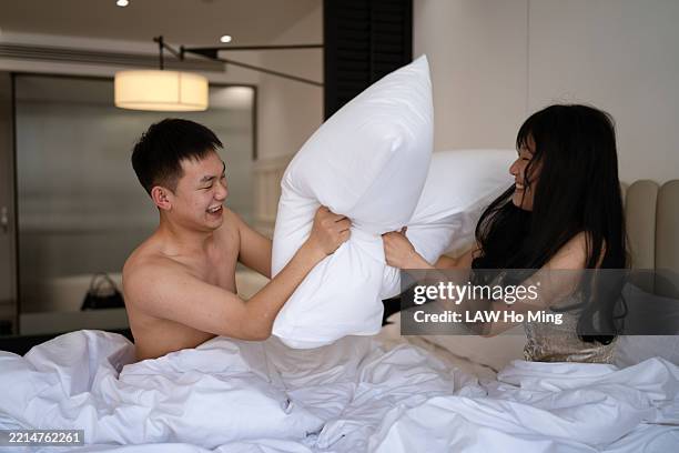 young couple having playful pillow fight in bed, joyful and energetic atmosphere - chinese pillow stock pictures, royalty-free photos & images