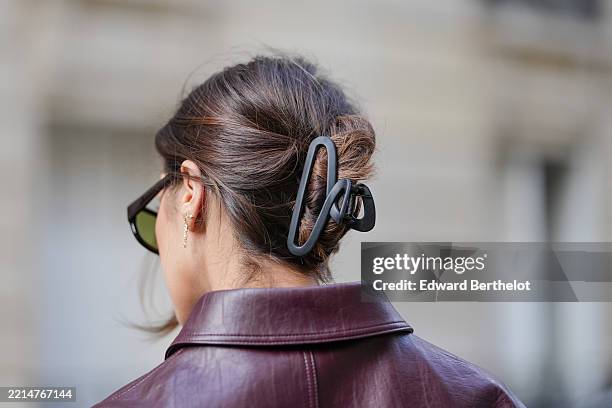 Close-up detail view of a large black matte plastic claw clip securing a twisted updo. Hair is styled in a loosely swept back look with long brown...