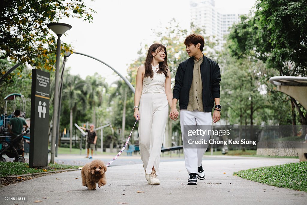 Pareja caminando de la mano con perro con correa en el parque"