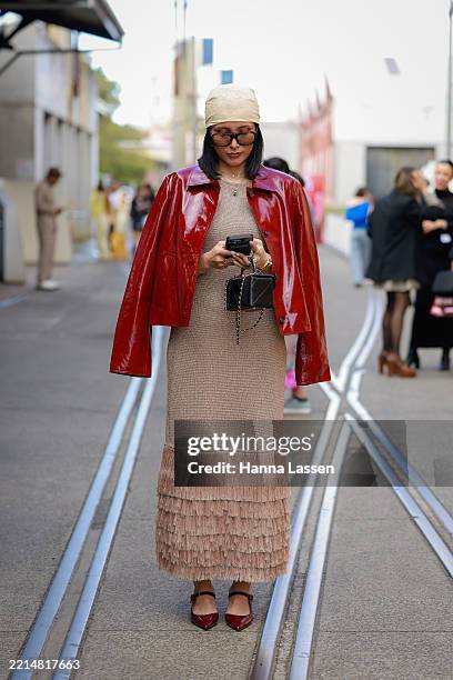 Guest wearing red patent jacket, fringed beige dress and burgundy shoes during Australian Fashion Week 2025 on May 13, 2025 in Sydney, Australia.