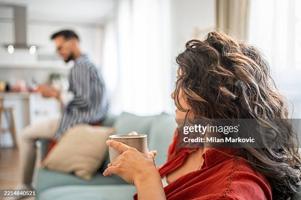 woman ignoring her partner while drinking coffee on the sofa - distant stock pictures, royalty-free photos & images