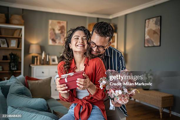 giovane che sorprende la sua ragazza con un regalo e fiori a casa - san valentino festività pubblica foto e immagini stock