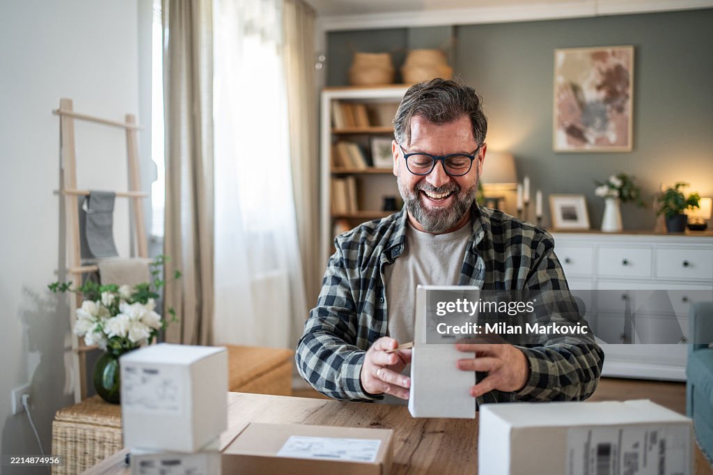 Happy mature man opening packages at home