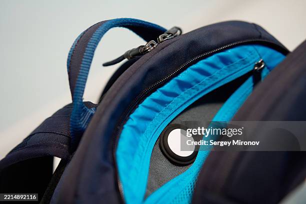 gps tracker airtag hidden inside the front compartment of a blue backpack with open zipper on a light background - location tracking stock pictures, royalty-free photos & images