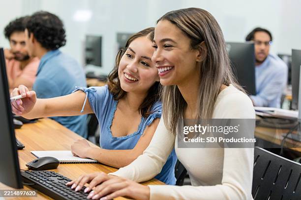 dos mujeres jóvenes colaboran en una computadora portátil en un laboratorio de computación - laboratorio de ordenadores fotografías e imágenes de stock