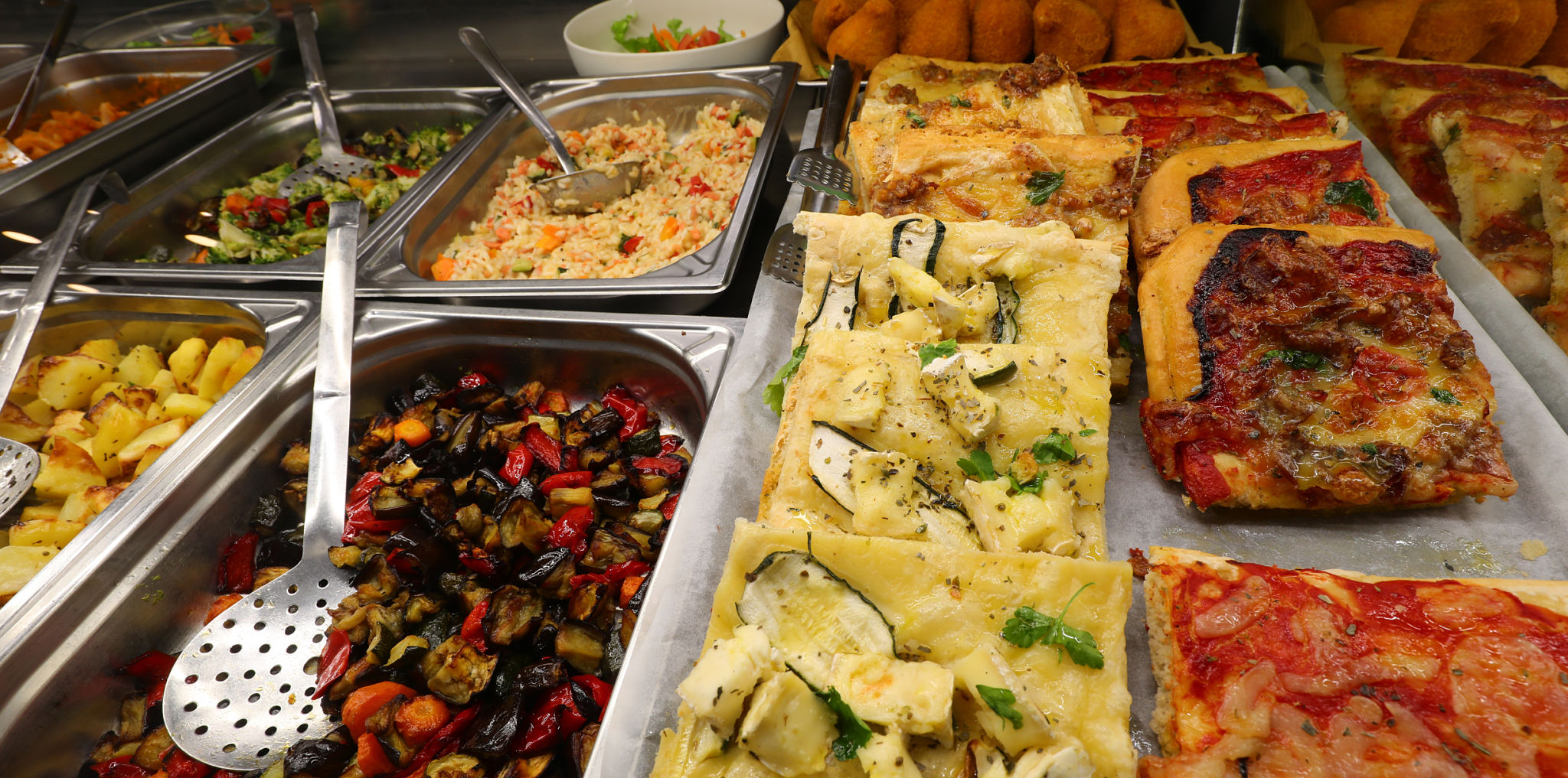 very full trays with hot dishes such as vegetable salad pizza and focaccia in the self-service very full trays with hot dishes such as vegetable salad pizza and focaccia in the self-service