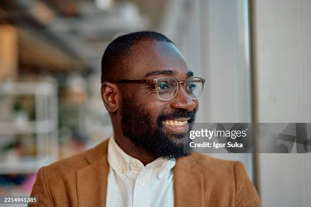 young african american businessman smiling and looking outside the window - formal businesswear stock pictures, royalty-free photos & images