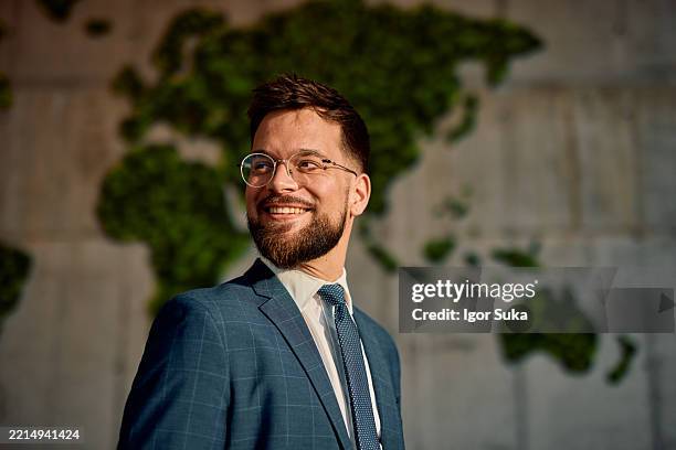 lächelnder geschäftsmann, der mit weltkarte im hintergrund wegschaut - grüner anzug stock-fotos und bilder