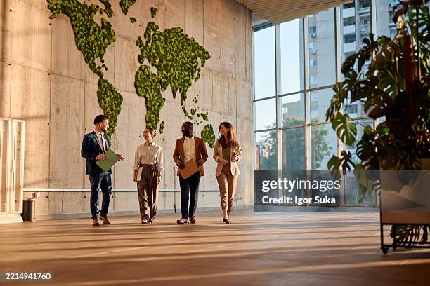 des hommes d’affaires marchent et discutent dans un bureau moderne avec une carte du monde verte - communication globale photos et images de collection
