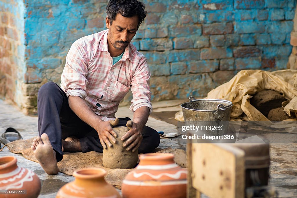Indian potter man kneading clay and preparing it for work on a pottery wheel.