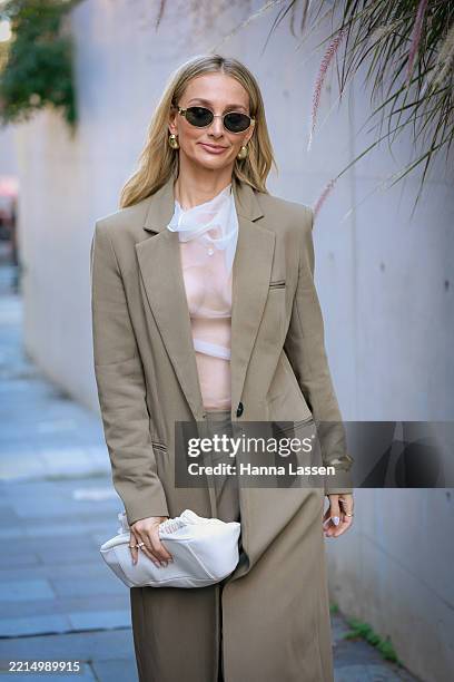 Anna Heinrich wearing white sheer top, beige coat, beige wide pants and white clutch during Australian Fashion Week 2025 on May 14, 2025 in Sydney,...
