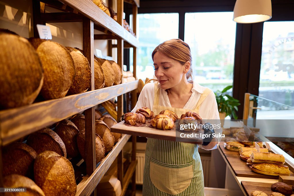 Baker smelling freshly baked cinnamon rolls in bakery shop