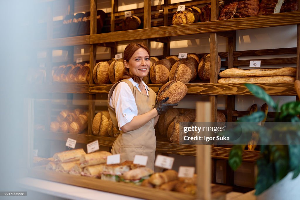 Smiling baker woman holding loaf of bread in bakery shop