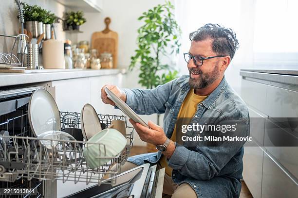 happy man emptying dishwasher in modern kitchen - washing dishes stock pictures, royalty-free photos & images