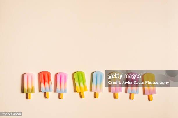 colorful popsicles arranged in a row on a beige background - fila arranjo imagens e fotografias de stock