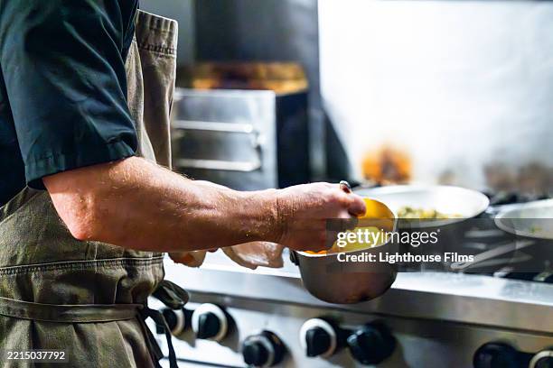 a chef holds a bowl of bright yellow sauce infront of a metal gas stove. - sauce stock pictures, royalty-free photos & images