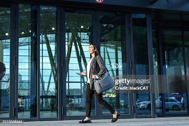 professional woman walking confidently with laptop bag near a modern public station - laptop bag stock pictures, royalty-free photos & images