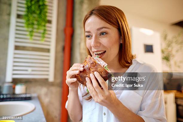 young woman enjoying a tasty sandwich in her kitchen - pork stock pictures, royalty-free photos & images