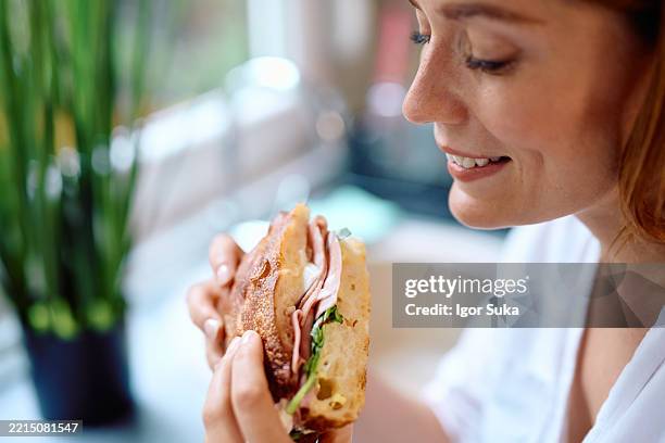 young woman enjoying a tasty sandwich at home - ciabatta stockfoto's en -beelden