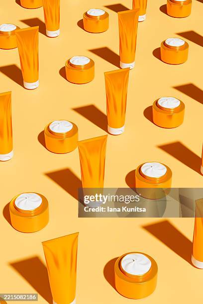 face cream, suntan lotion, hair conditioner in gold tubes, jars on yellow, orange color background. cosmetic products for makeup, skincare and uv protection. 3d vertical pattern. - toiletries stock pictures, royalty-free photos & images