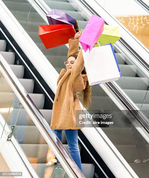 young woman holding shopping bags on escalator in mall - kaufsucht stock-fotos und bilder