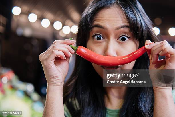 young asian woman holding chili pepper like mustache at the market - roter chili stock-fotos und bilder