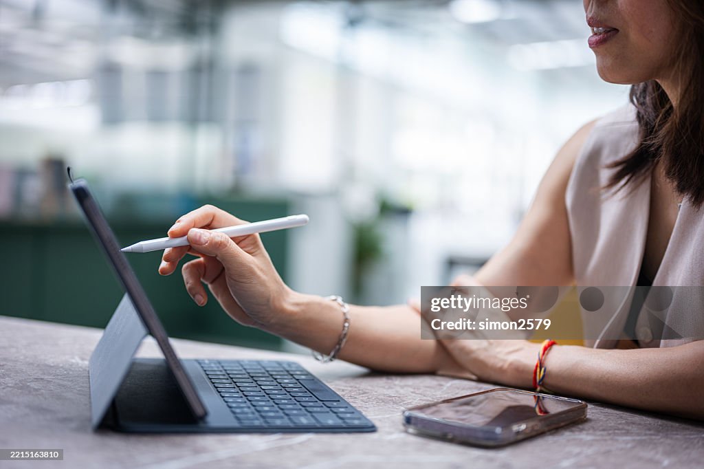 An Asian businesswoman works on a business plan using a stylus pen on a tablet screen in the office