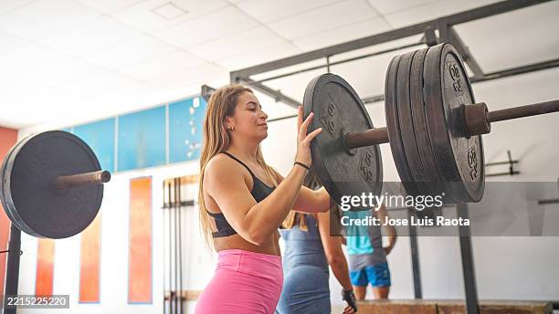 woman in gym, carefully placing weight plates on dumbbells before starting her workout - barbell stock pictures, royalty-free photos & images