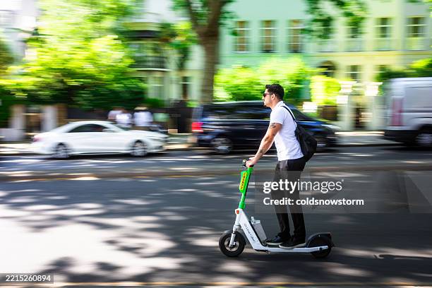 blurred motion of man riding lime e-scooter on road in central london, uk - elektrische step stockfoto's en -beelden