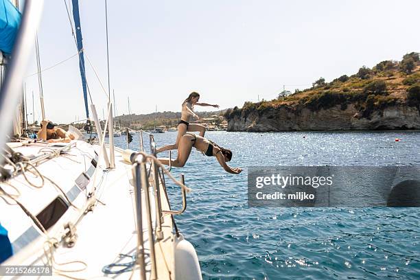 zwei junge frauen springen von einem segelboot ins meer - schiffsdeck stock-fotos und bilder
