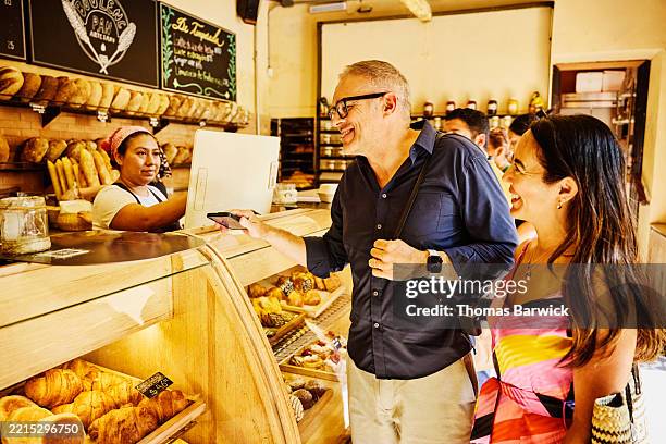 medium wide shot senior couple ordering snacks at local bakery - voyage expérientiel photos et images de collection
