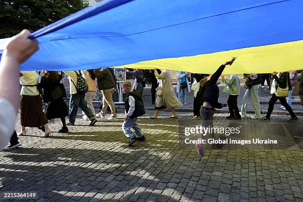 Children play under a large Ukrainian flag carried by people along Derybasivska Street during the Vyshyvanka Day celebration on May 15, 2025 in...