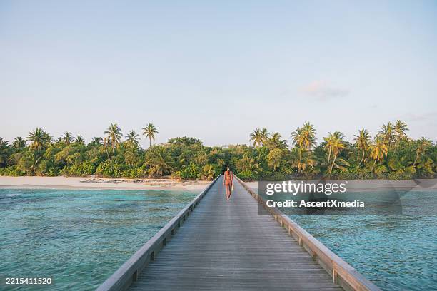 giovane donna cammina lungo la passerella sopra la laguna tropicale - esotismo foto e immagini stock