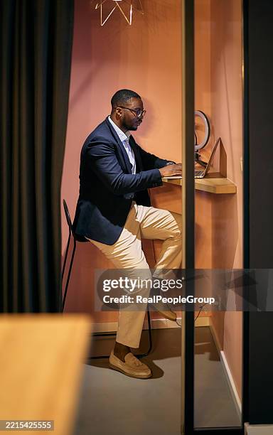 focused businessman working on laptop in modern office phone booth - telephone booth stock pictures, royalty-free photos & images
