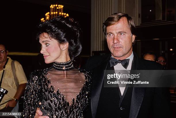 American actress Connie Sellecca, wearing a black sequin evening gown with a sheer neckline panel, and her husband, American actor Gil Gerard, who...