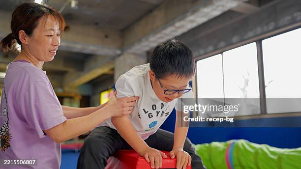 niño con síndrome de down haciendo actividades físicas con un instructor en el aula de actividad física - discapacidad del desarrollo fotografías e imágenes de stock