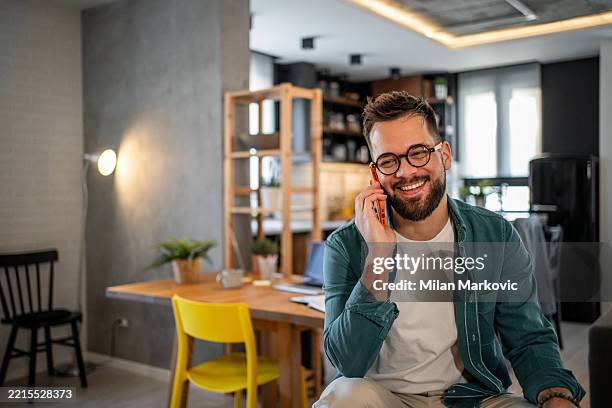 young man smiling while talking on the phone at home - einzelner mann über 30 stock-fotos und bilder