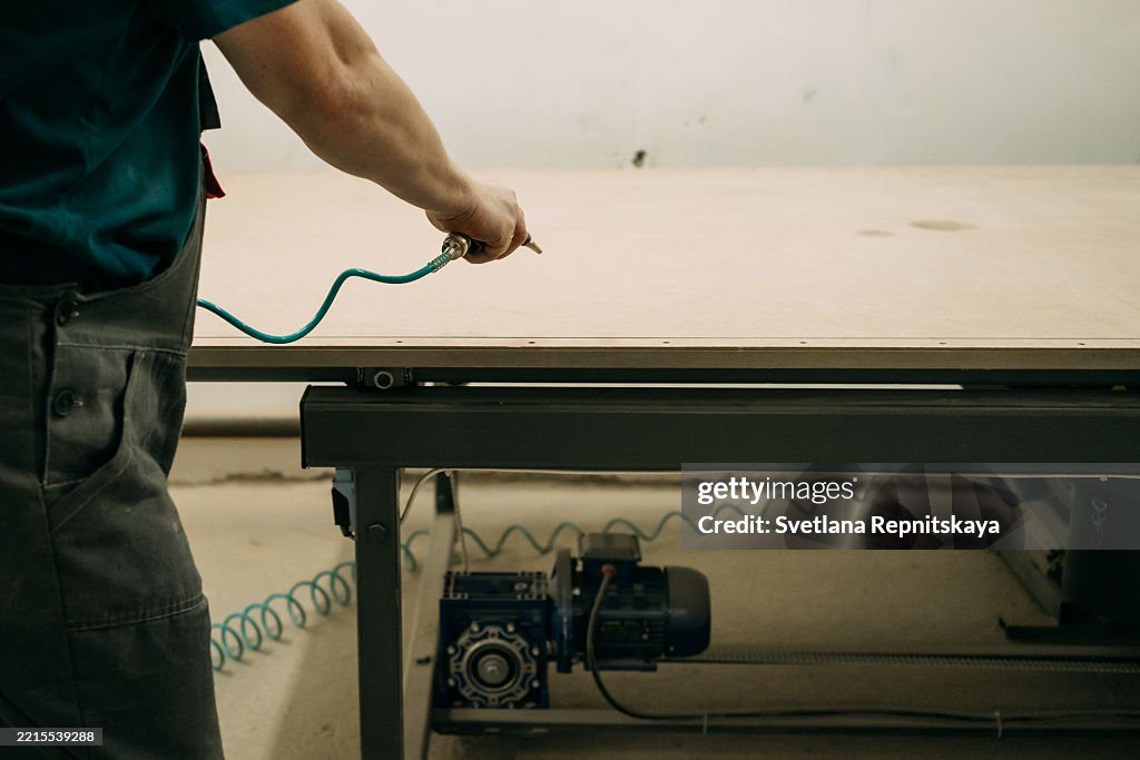 Carpenter using pneumatic tool on wooden plank in workshop
