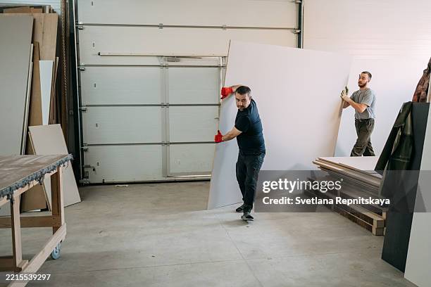 two carpenters moving large panel in workshop - planche de bois photos et images de collection