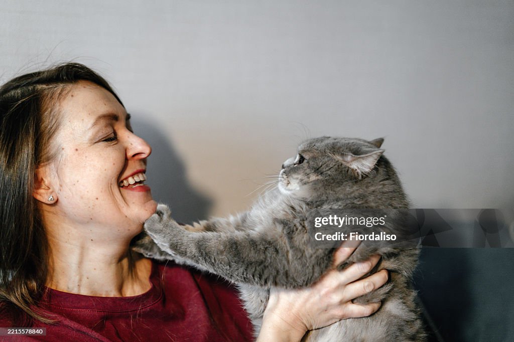 Smiling woman engaging playfully with her adorable gray pet cat