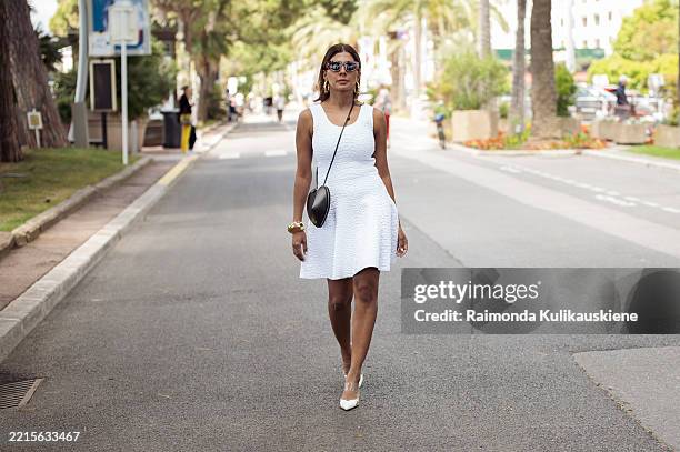 Zufi Alexander wears white mini dress from Alaia, black heart shape bag from Alaia, big golden statement bracelet and white pointy shoes and Loewe...