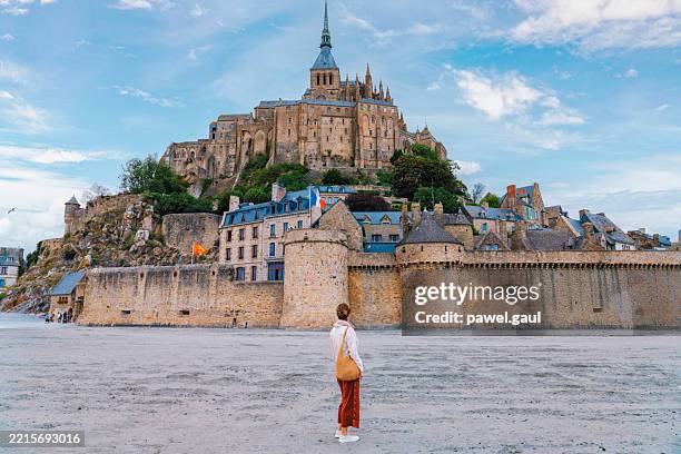 mont saint-michel, un'abbazia medievale e un villaggio su un'isola rocciosa in normandia, in francia, con una persona in piedi in primo piano. - mont saint michel foto e immagini stock